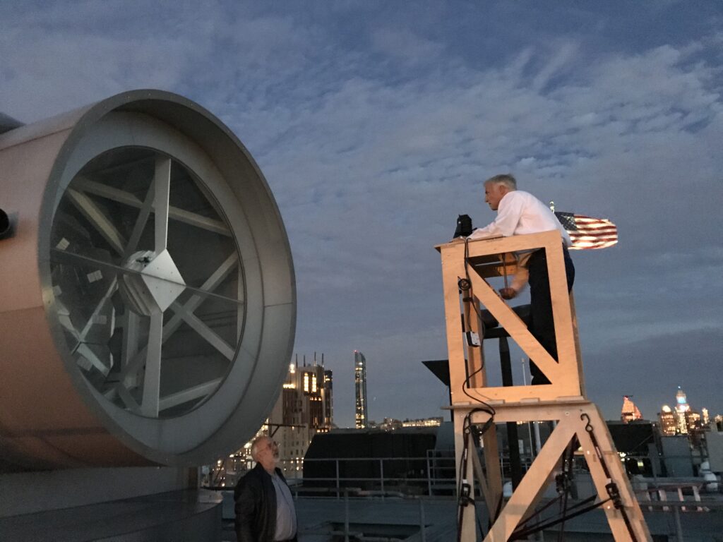 man standing in cherry picker basket looking into a solar telescope atop a high rise in manhattan