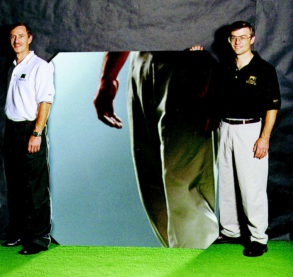 2 men standing next to a square mirror with chamfered corners